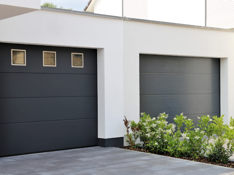 Dwa garaże połączone ze sobą. Jedna brama garażowa z trzema okienkami. Druga bez okien.